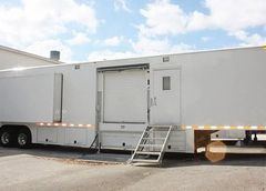 White mobile medical unit with entrance ramp and overhead lighting mounted on a multi-axle trailer